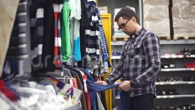 成人戴眼镜，穿衬衫，在商店里选择羊绒衫。